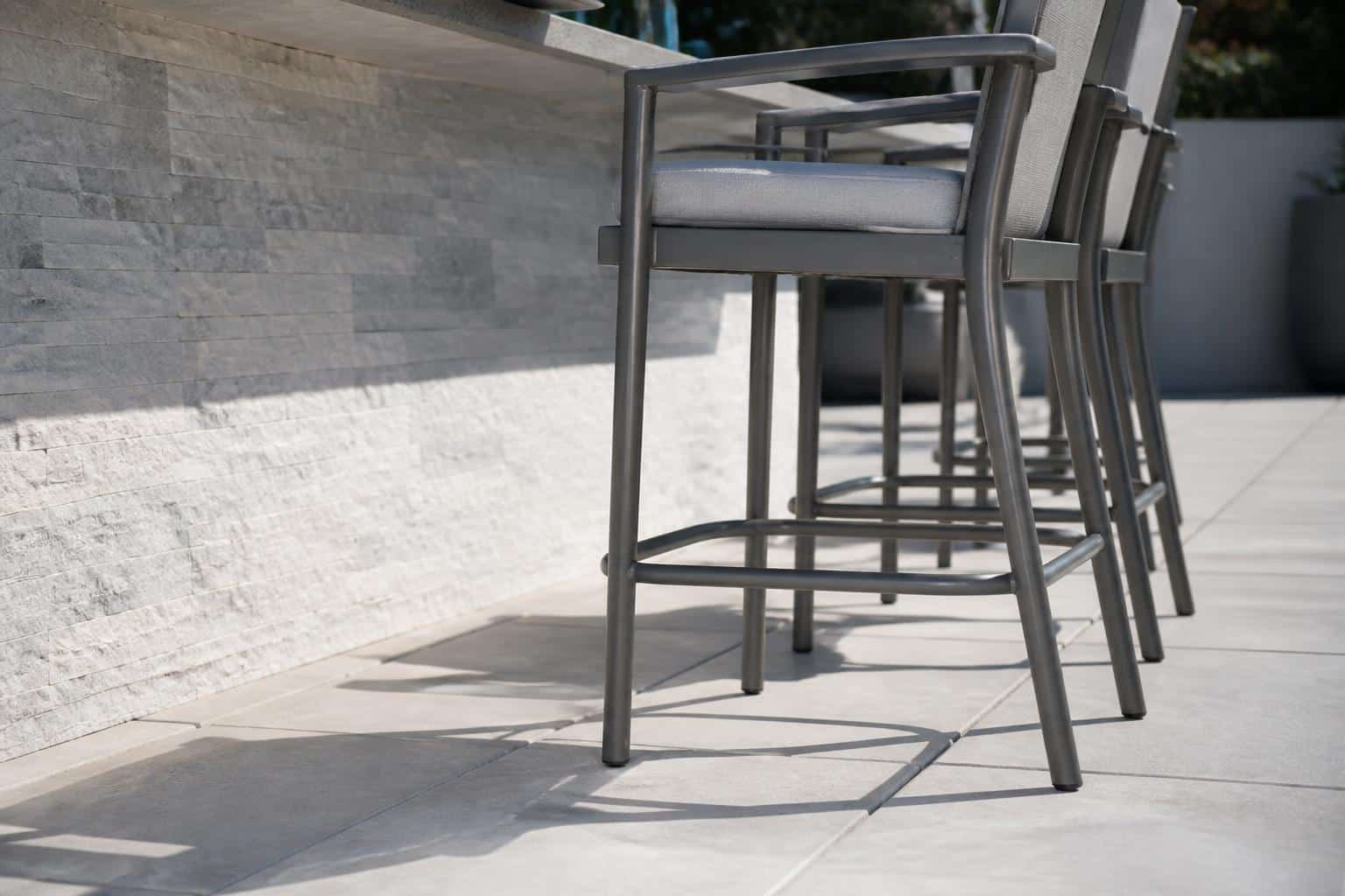 Close view of an outdoor counter-height stool showing seat clearance under a stone bar and a horizontal footrest rung