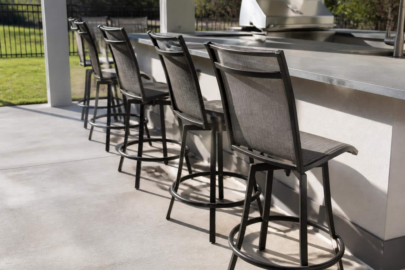 Wide view of a Charlotte outdoor kitchen with four bar-height stools evenly spaced along a stone counter