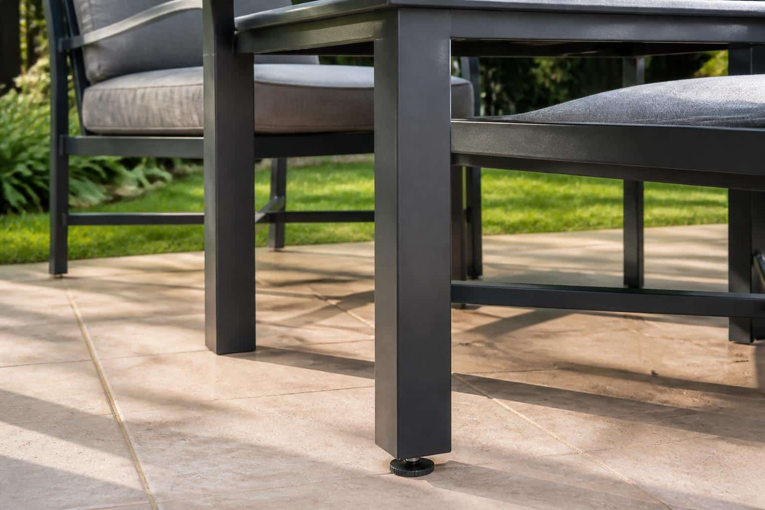 Close view of an adjustable threaded glide beneath an aluminum patio table leg on brick pavers