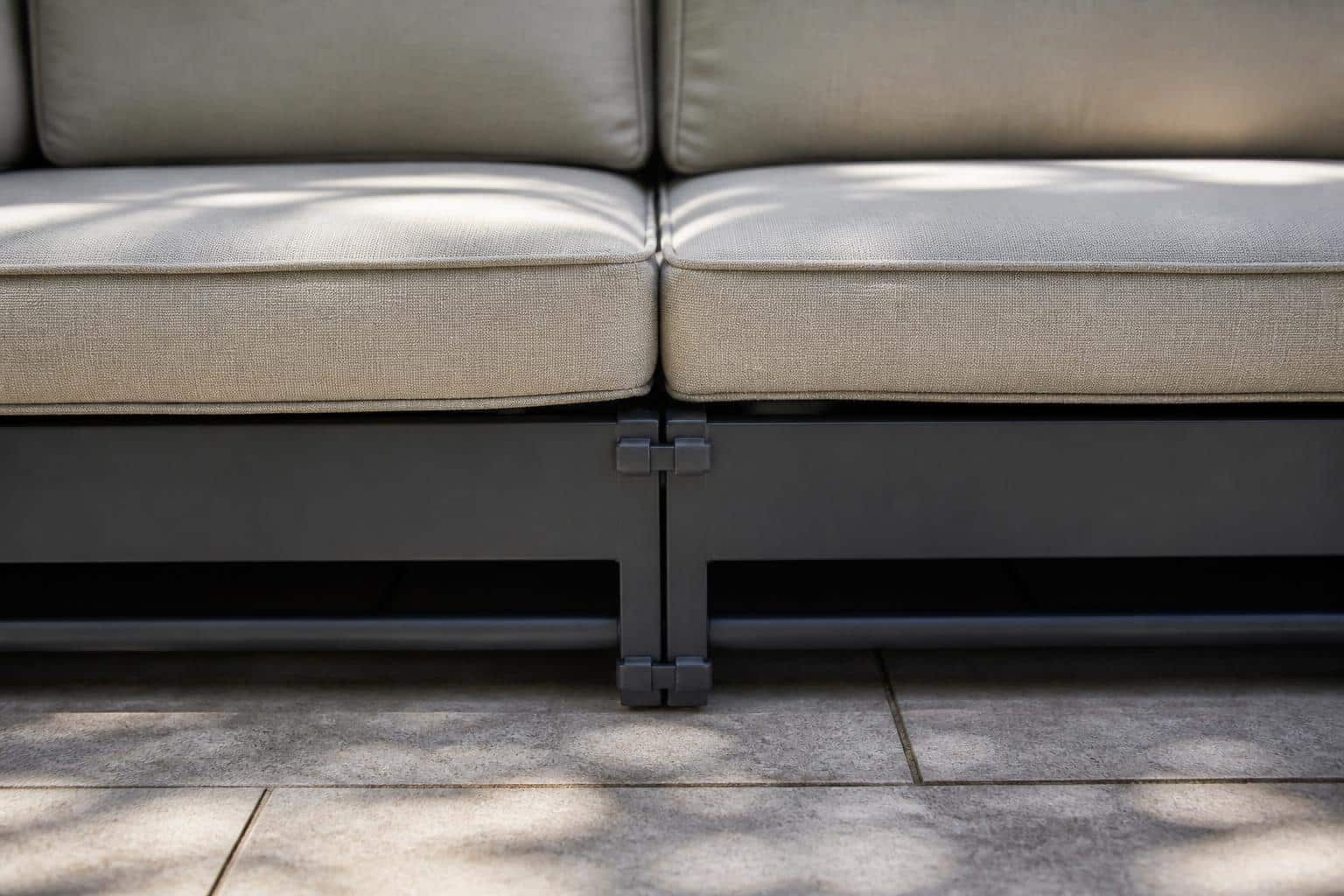 Close view of a metal connector bracket joining two modular outdoor sofa frames on a residential patio