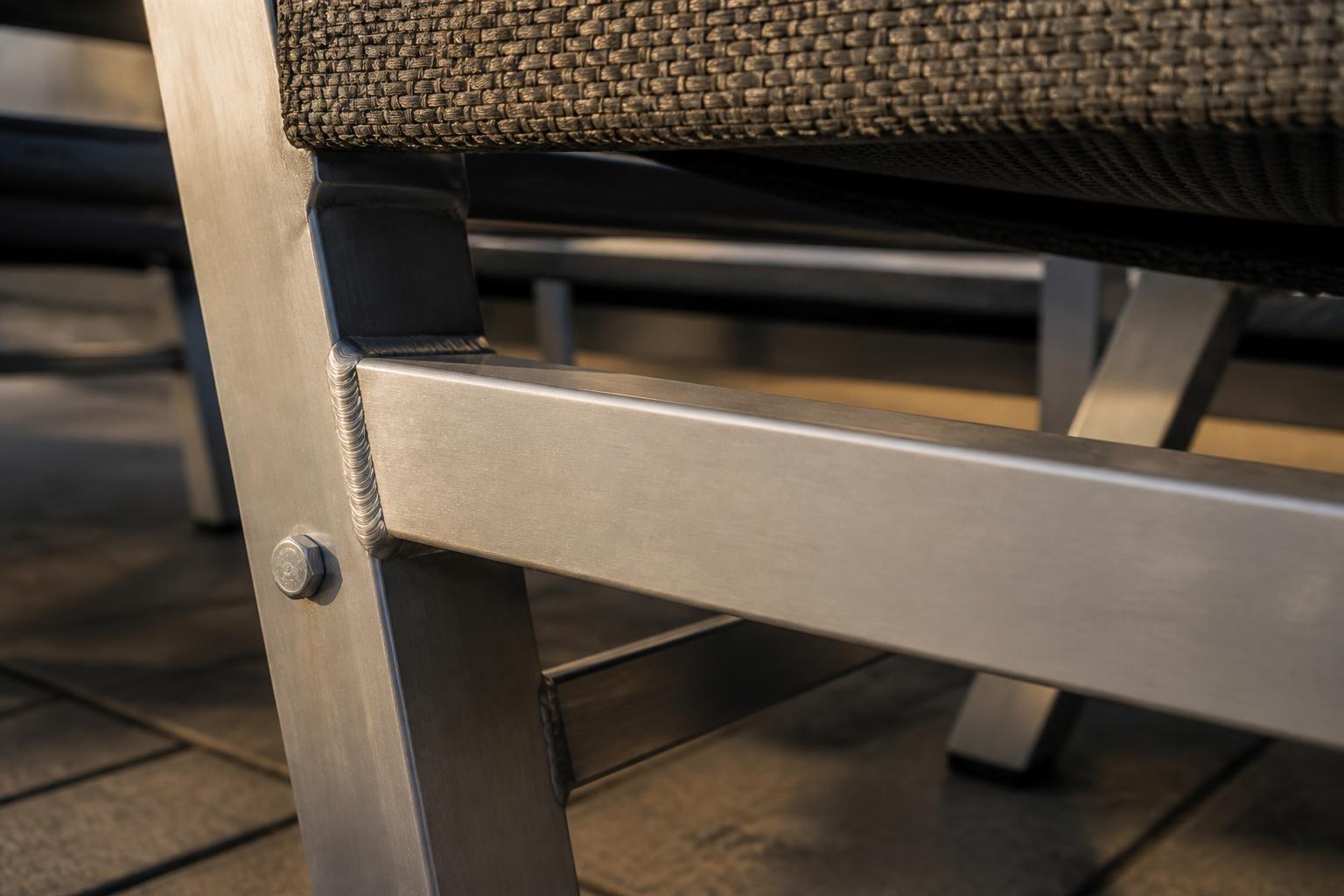 Close-up of a welded and bolted aluminum chair frame joint beneath a woven outdoor seat
