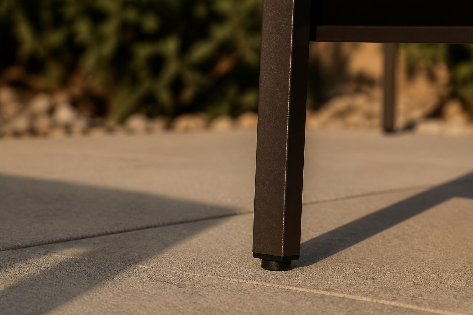 Dark bronze aluminum patio table leg with a smooth even finish and a rubber foot on a concrete patio